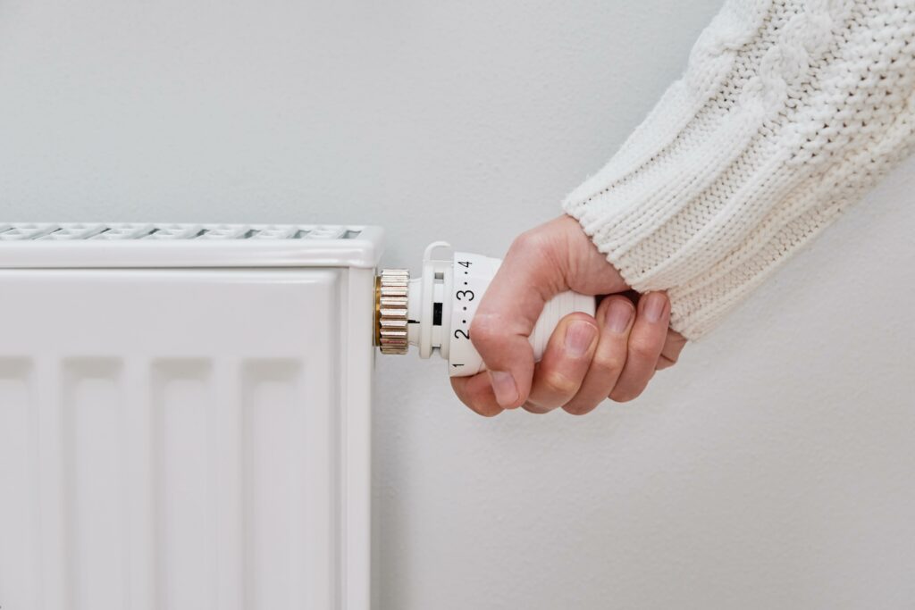 Person die am Thermostat der Heizung dreht