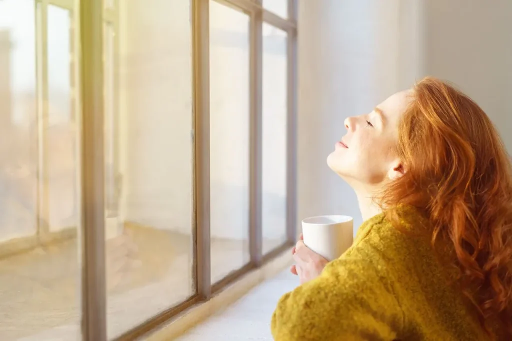 Frau genießt die Sonne und sitzt am Fenster