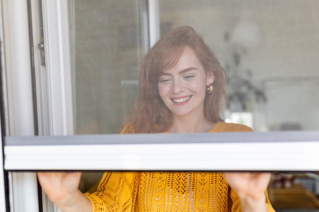 junge Frau öffnet Insektenschutz für Fenster